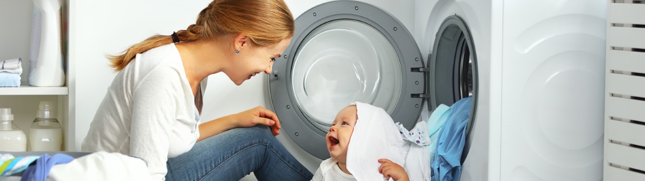 תמונה של אמא ותינוק משחקים בכביסה נקיה ליד מייבש כביסה